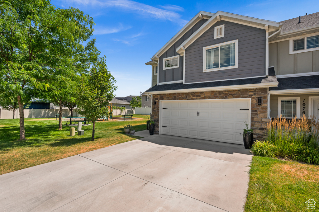 View of front facade with board and batten siding, a garage, stone siding, and driveway