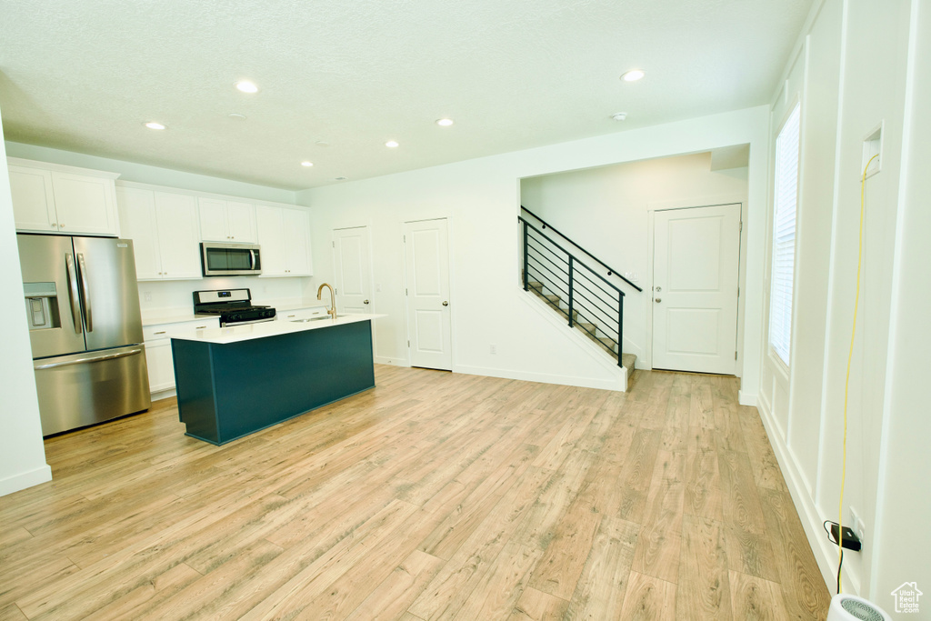 Kitchen with stainless steel appliances, an island with sink, recessed lighting, white cabinetry, and light wood-style flooring