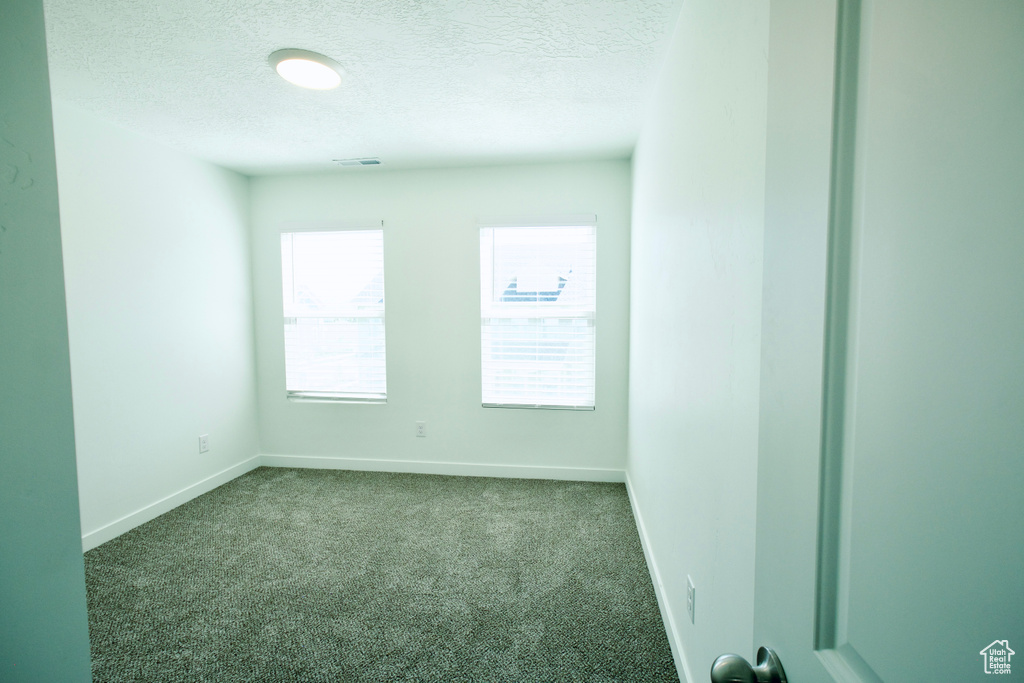 Empty room with a textured ceiling and dark carpet