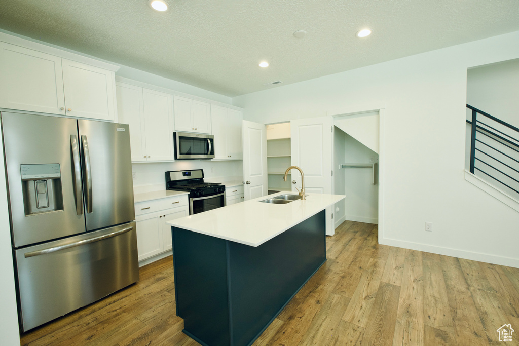 Kitchen featuring appliances with stainless steel finishes, white cabinets, a center island with sink, light countertops, and recessed lighting