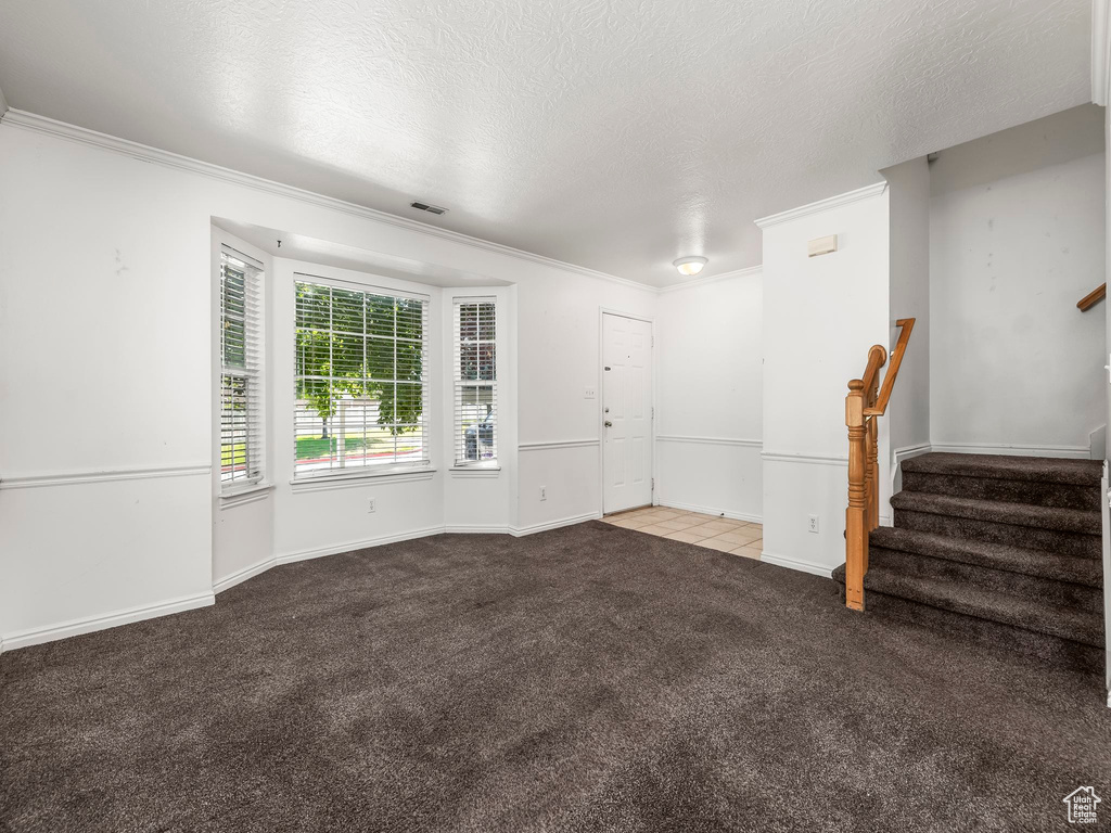 Unfurnished living room featuring carpet floors, stairs, crown molding, and a textured ceiling