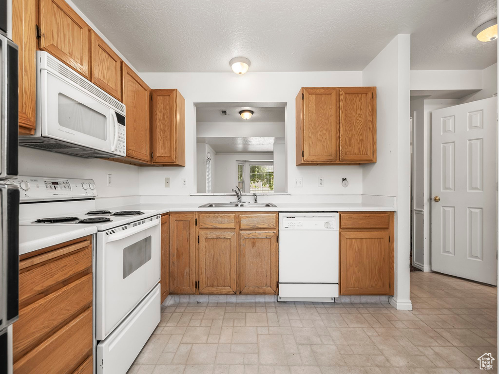Kitchen with white appliances, light countertops, and brown cabinetry