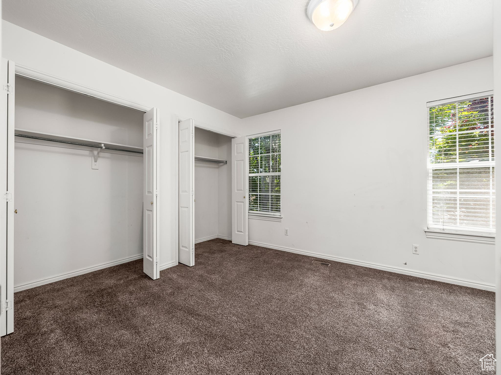 Unfurnished bedroom with two closets and dark colored carpet