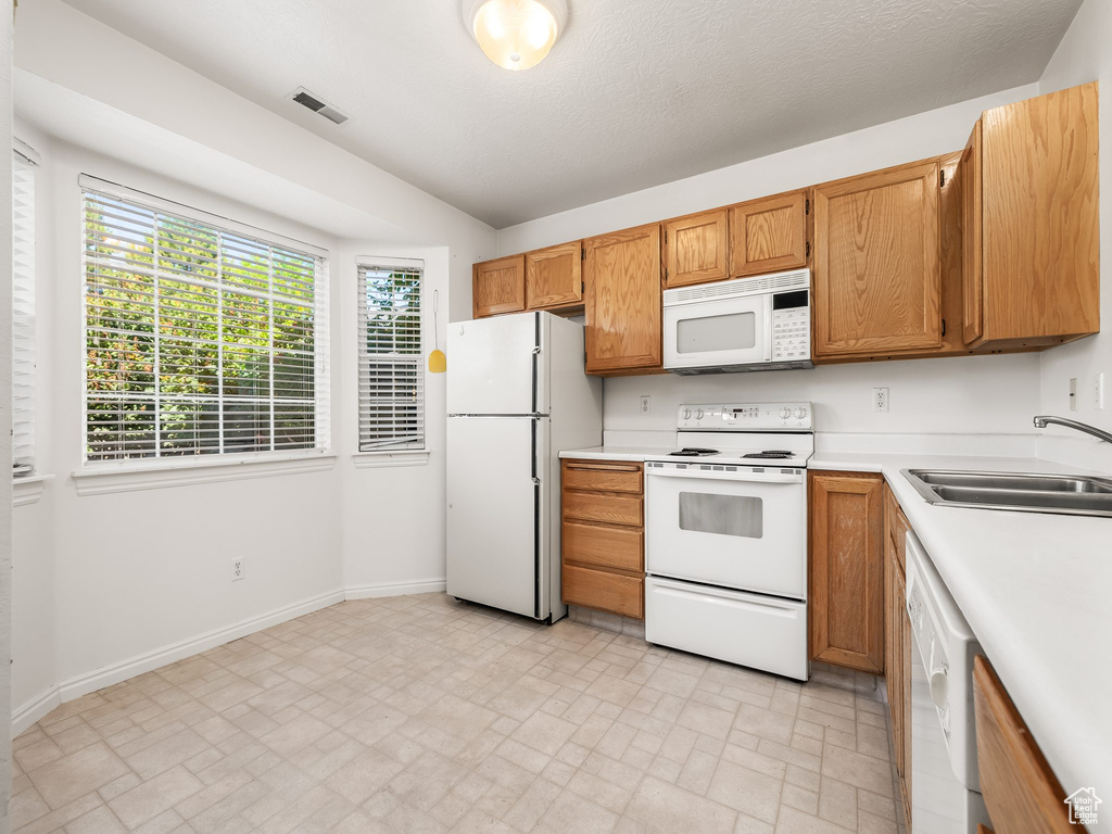 Kitchen featuring white appliances, light countertops, brick patterned floors, and brown cabinets