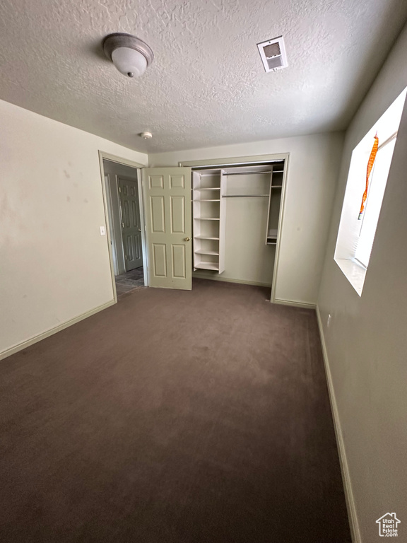 Unfurnished bedroom with a textured ceiling, carpet flooring, and a closet