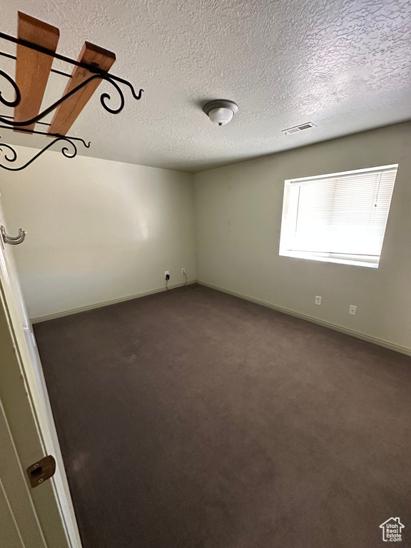 Empty room with a textured ceiling and dark colored carpet