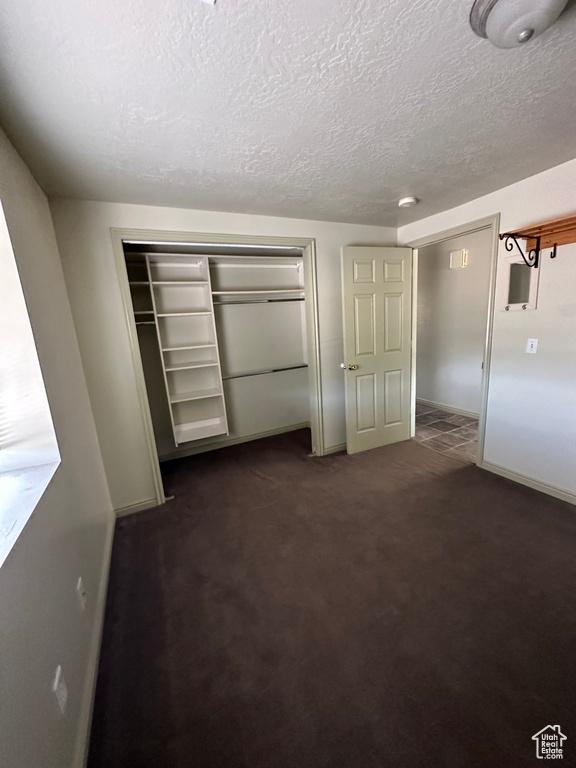 Unfurnished bedroom featuring a closet, a textured ceiling, and dark colored carpet