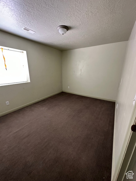 Empty room with dark carpet and a textured ceiling