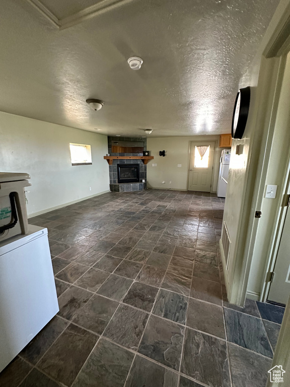 Unfurnished living room featuring a textured ceiling, a fireplace, and dark stone finish flooring
