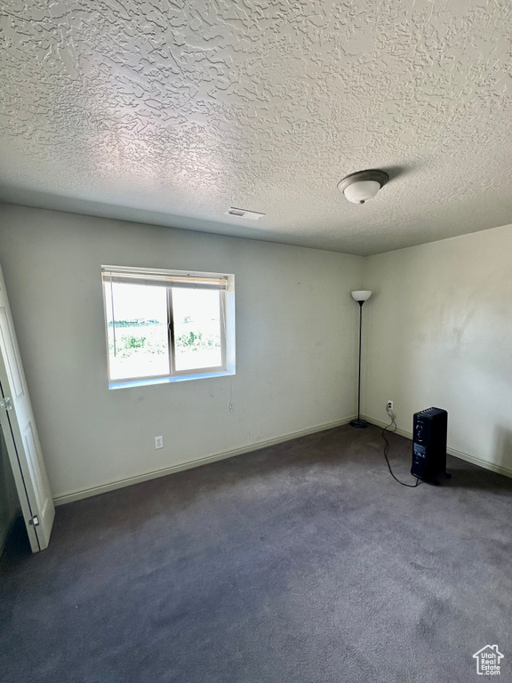 Empty room with dark colored carpet and a textured ceiling