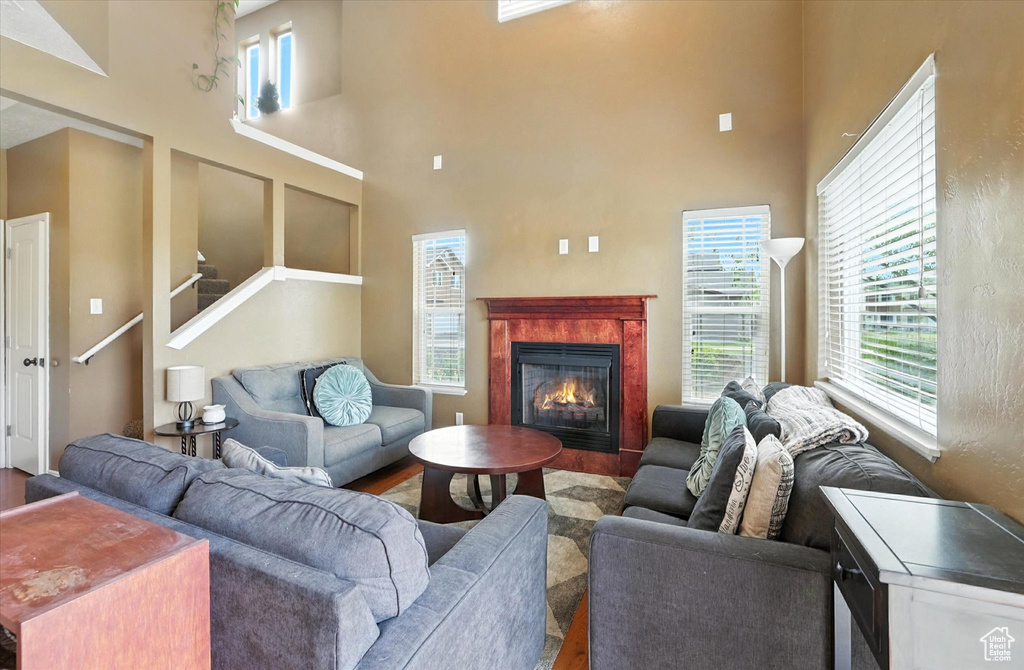 Living area with wood finished floors, a high ceiling, healthy amount of natural light, a fireplace, and stairway