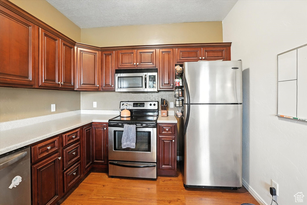 Kitchen featuring stainless steel appliances, light countertops, light wood finished floors, and a textured ceiling