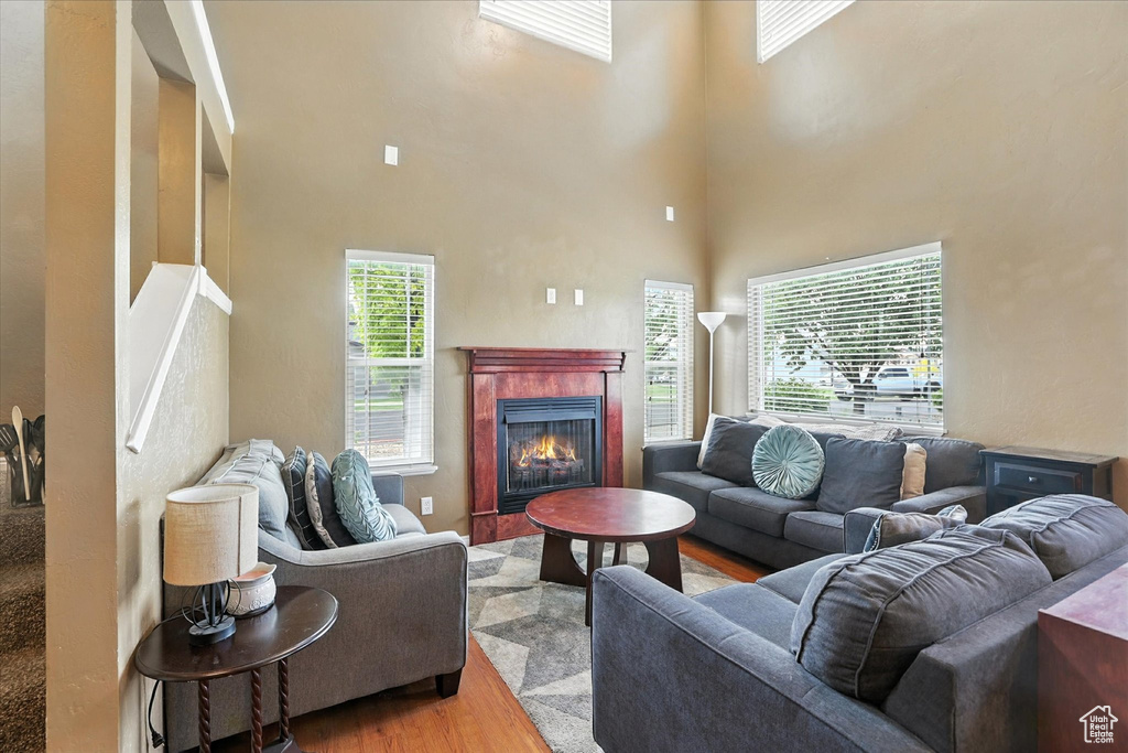 Living room with wood finished floors, a tiled fireplace, and a high ceiling