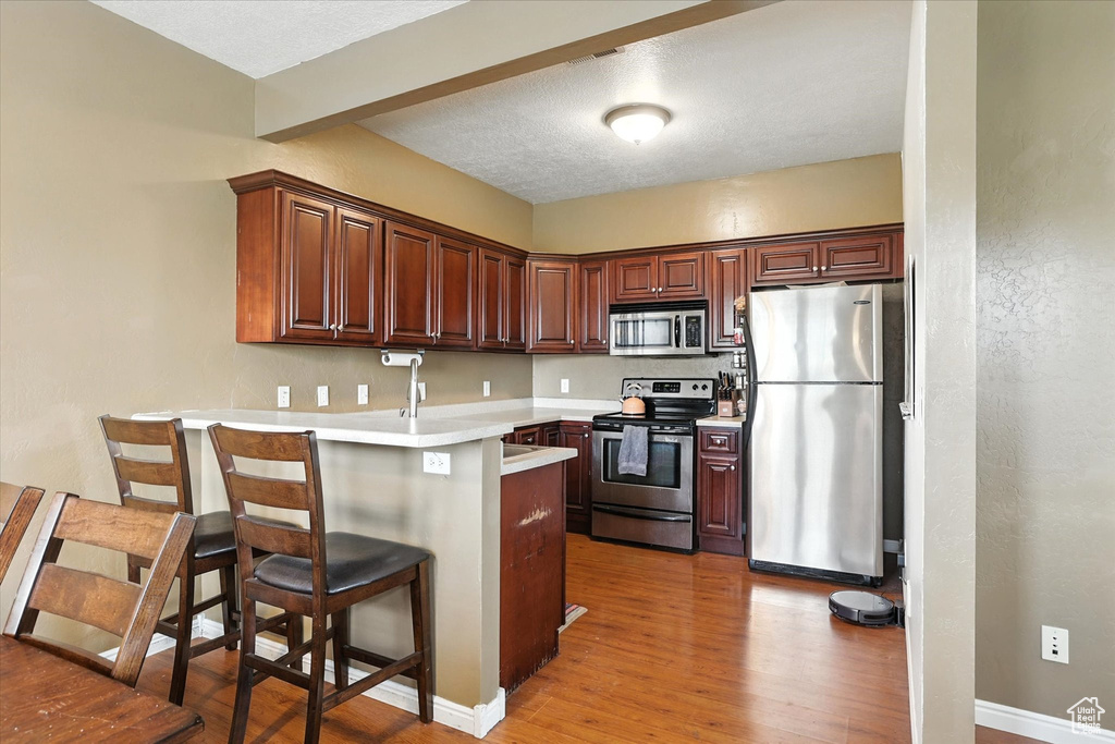 Kitchen with stainless steel appliances, a peninsula, light wood-style floors, a kitchen bar, and light countertops