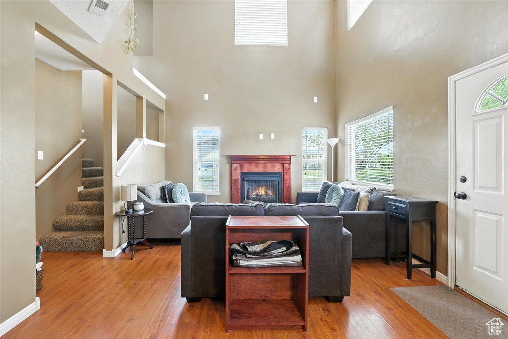 Living area featuring wood finished floors, a towering ceiling, healthy amount of natural light, stairway, and a tiled fireplace