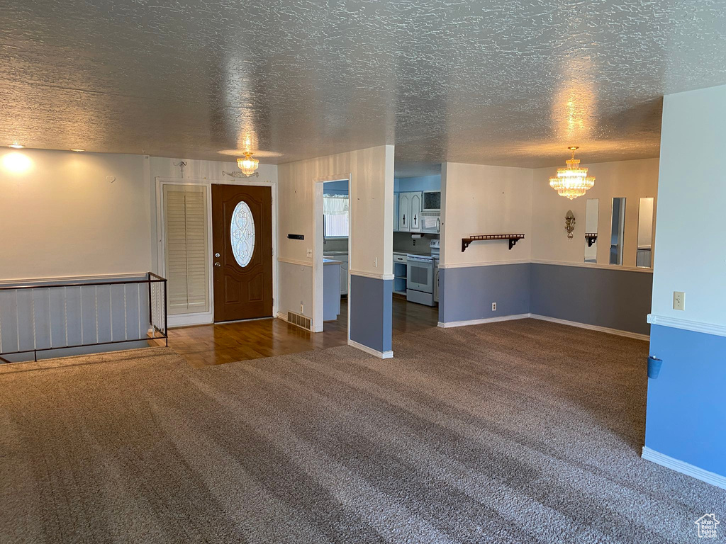 Foyer featuring dark colored carpet, a chandelier, and a textured ceiling