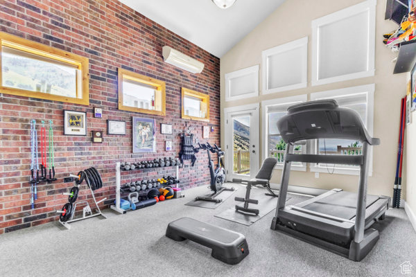 Exercise room with vaulted ceiling, carpet floors, and brick wall