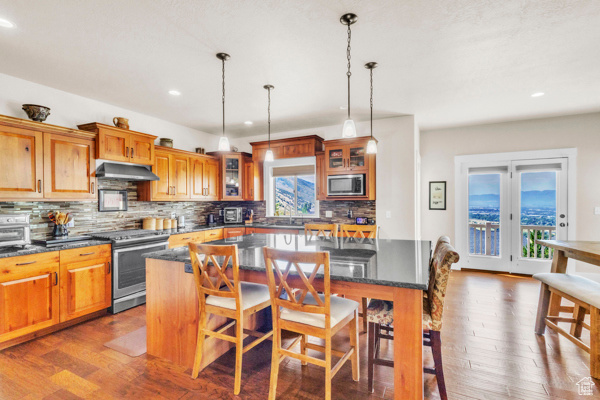 Kitchen with appliances with stainless steel finishes, recessed lighting, backsplash, ventilation hood, and a breakfast bar area