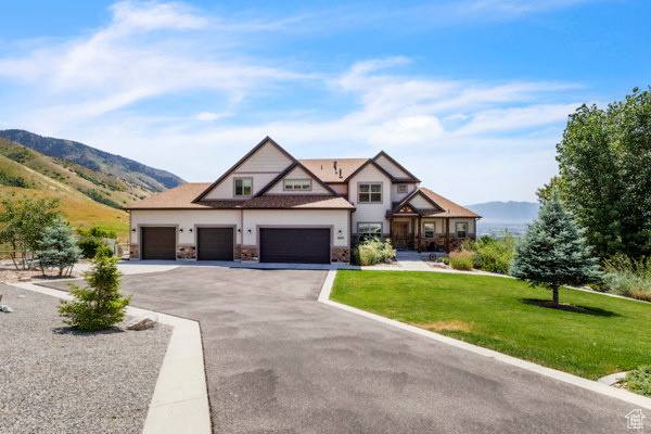 View of front facade with a mountain view, a front yard, driveway, stone siding, and a garage