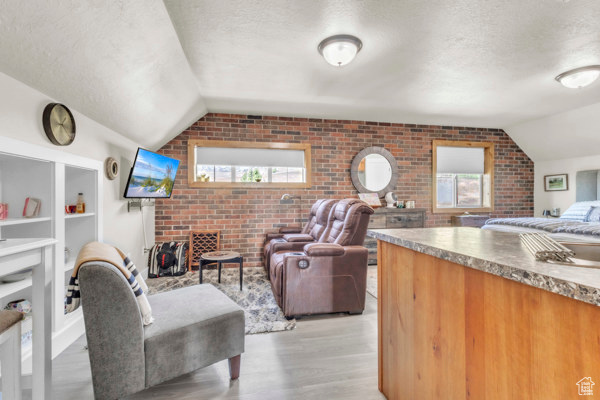 Living area with brick wall, vaulted ceiling, a textured ceiling, light wood-type flooring, and plenty of natural light