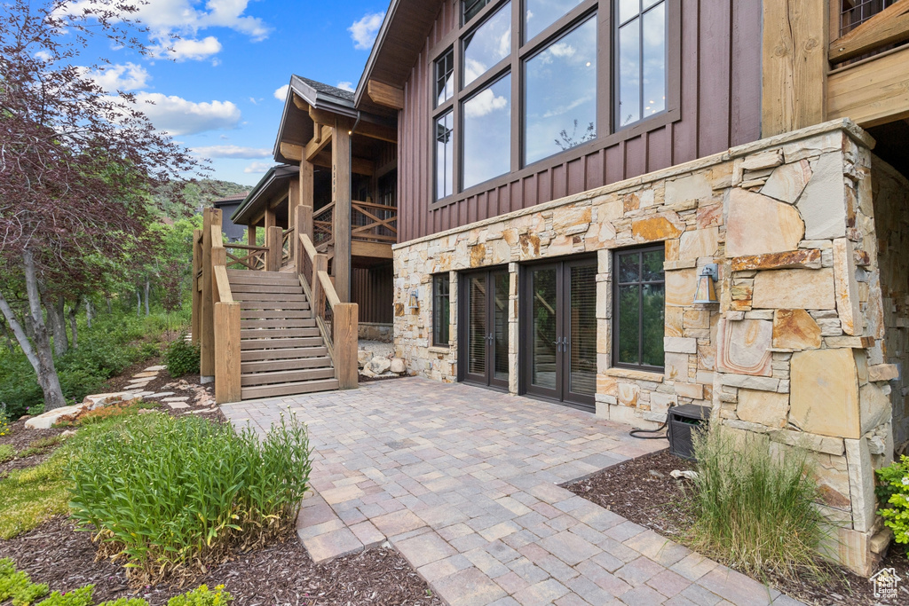 Rear view of house with stone siding, board and batten siding, stairway, and a patio