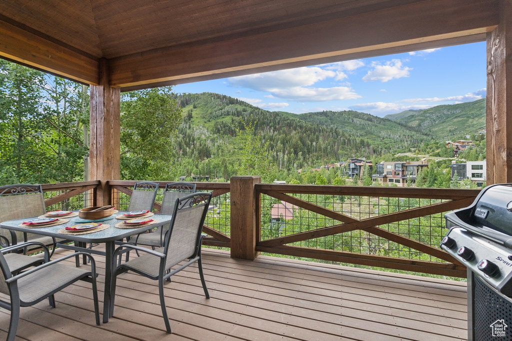 Wooden deck featuring a mountain view, outdoor dining area, grilling area, and a wooded view