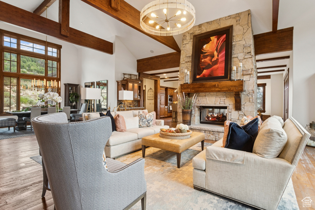 Living area with a chandelier, beam ceiling, high vaulted ceiling, a stone fireplace, and light wood-type flooring