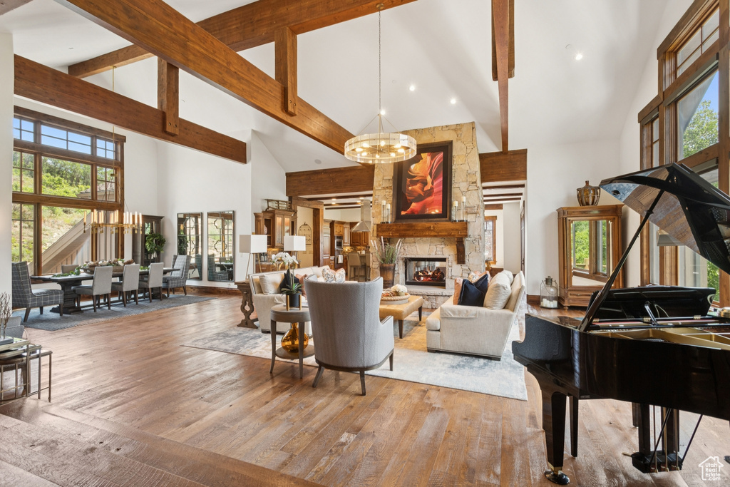 Living room featuring high vaulted ceiling, a chandelier, wood finished floors, beamed ceiling, and a stone fireplace