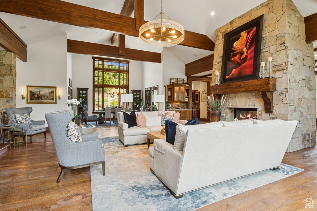 Living room featuring a stone fireplace, a chandelier, beam ceiling, high vaulted ceiling, and wood finished floors