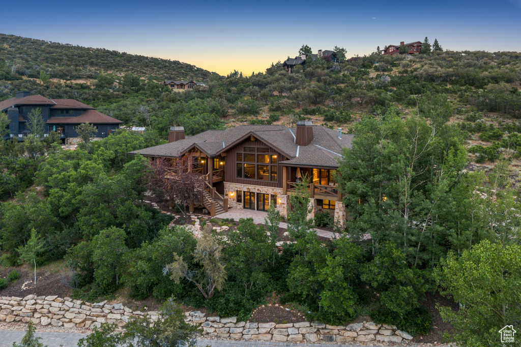 Back of property at dusk featuring stone siding, stairs, and a chimney