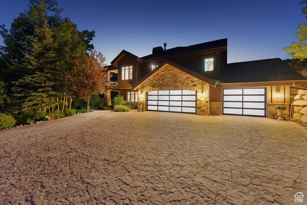 View of front of home featuring stone siding, decorative driveway, an attached garage, and a chimney