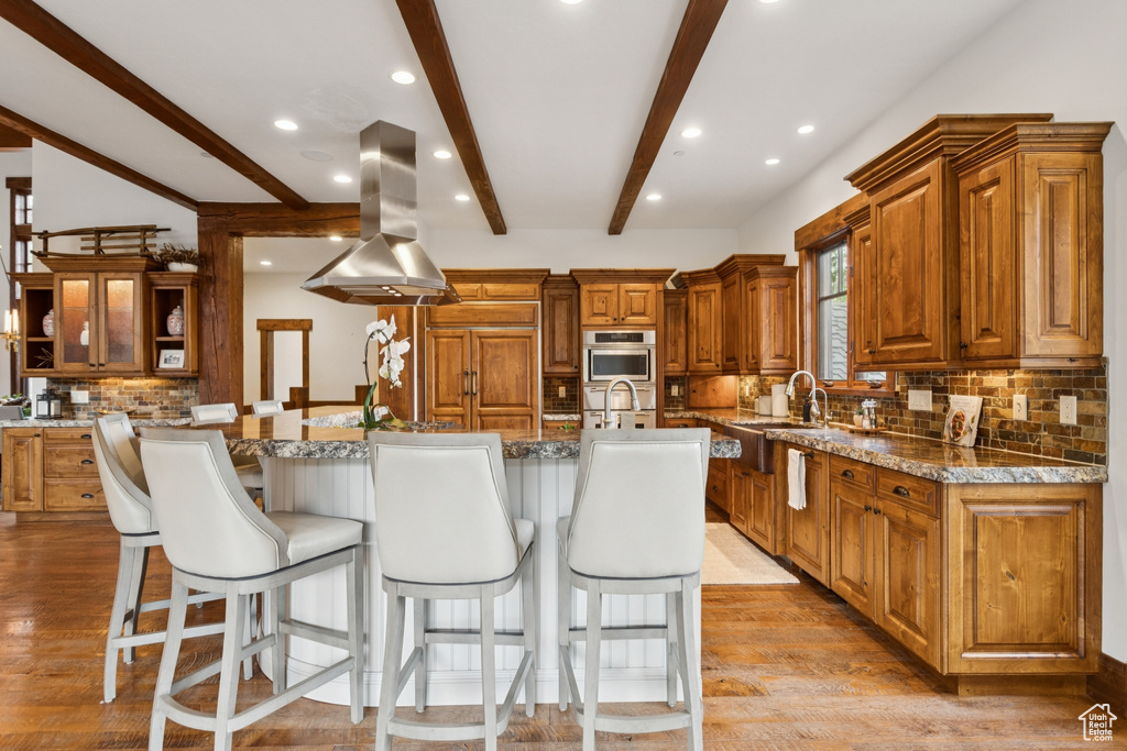 Kitchen with extractor fan, beamed ceiling, backsplash, a kitchen bar, and brown cabinetry