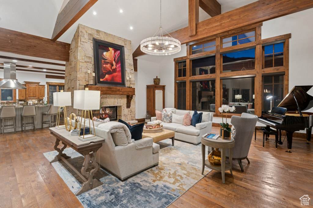 Living area featuring high vaulted ceiling, beam ceiling, hardwood / wood-style floors, a fireplace, and a chandelier