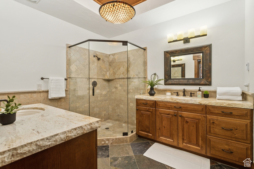 Bathroom featuring two vanities, a stall shower, tile walls, and a wainscoted wall
