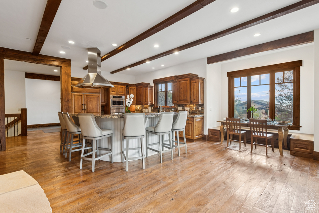 Kitchen with island range hood, beamed ceiling, recessed lighting, light wood-style flooring, and a breakfast bar