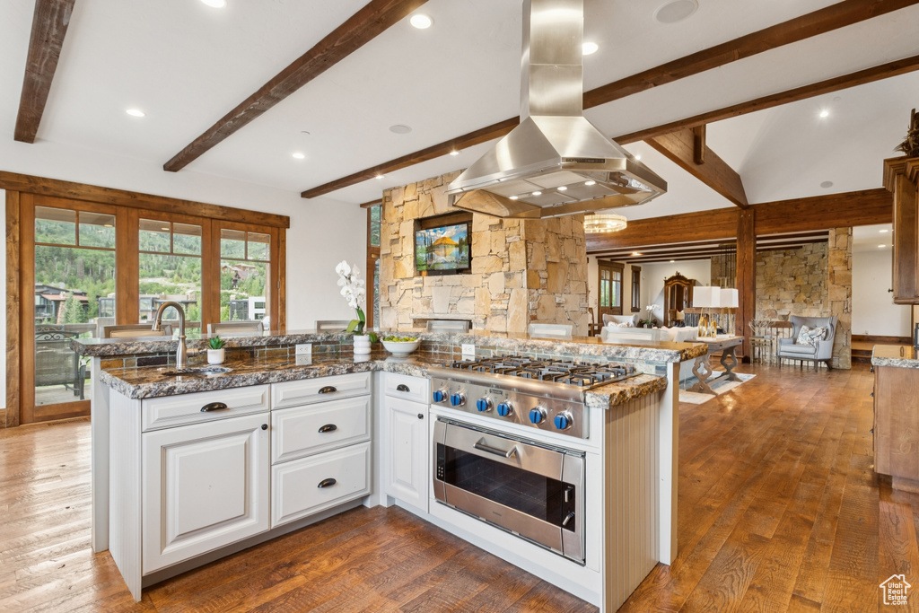 Kitchen with island range hood, beamed ceiling, white cabinets, appliances with stainless steel finishes, and wood finished floors