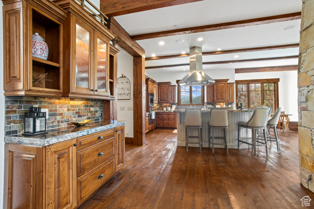 Kitchen featuring dark wood finished floors, a breakfast bar area, brown cabinetry, tasteful backsplash, and beam ceiling