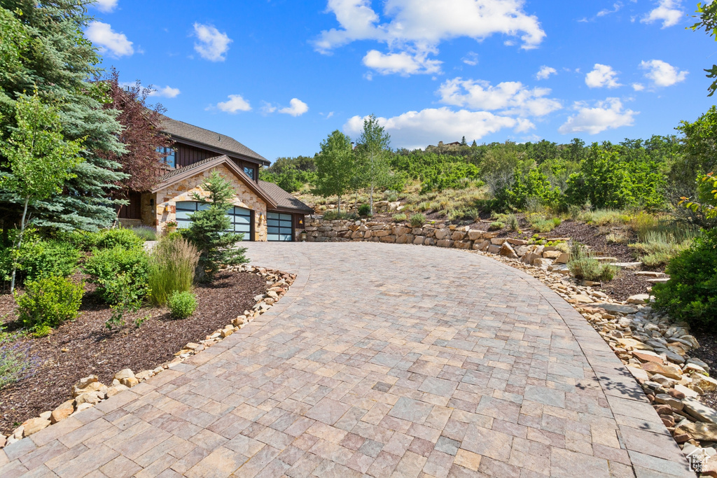 View of side of property featuring a garage, stone siding, and decorative driveway