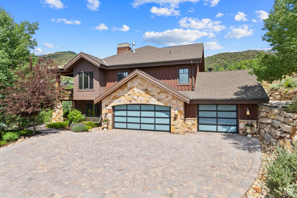 View of front of property with stone siding, board and batten siding, a chimney, a garage, and decorative driveway