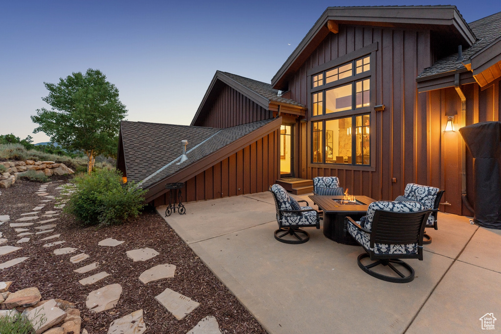 Rear view of house featuring board and batten siding, a shingled roof, a fire pit, and a patio area