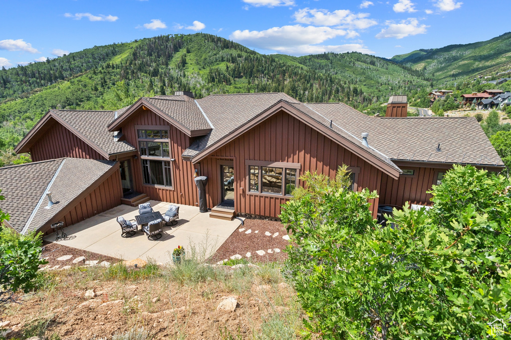 Back of property with board and batten siding, a mountain view, a patio area, and a chimney