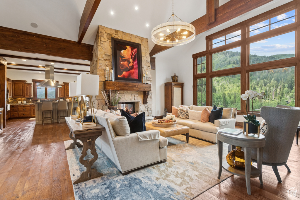 Living room featuring beamed ceiling, a towering ceiling, wood-type flooring, a chandelier, and a fireplace