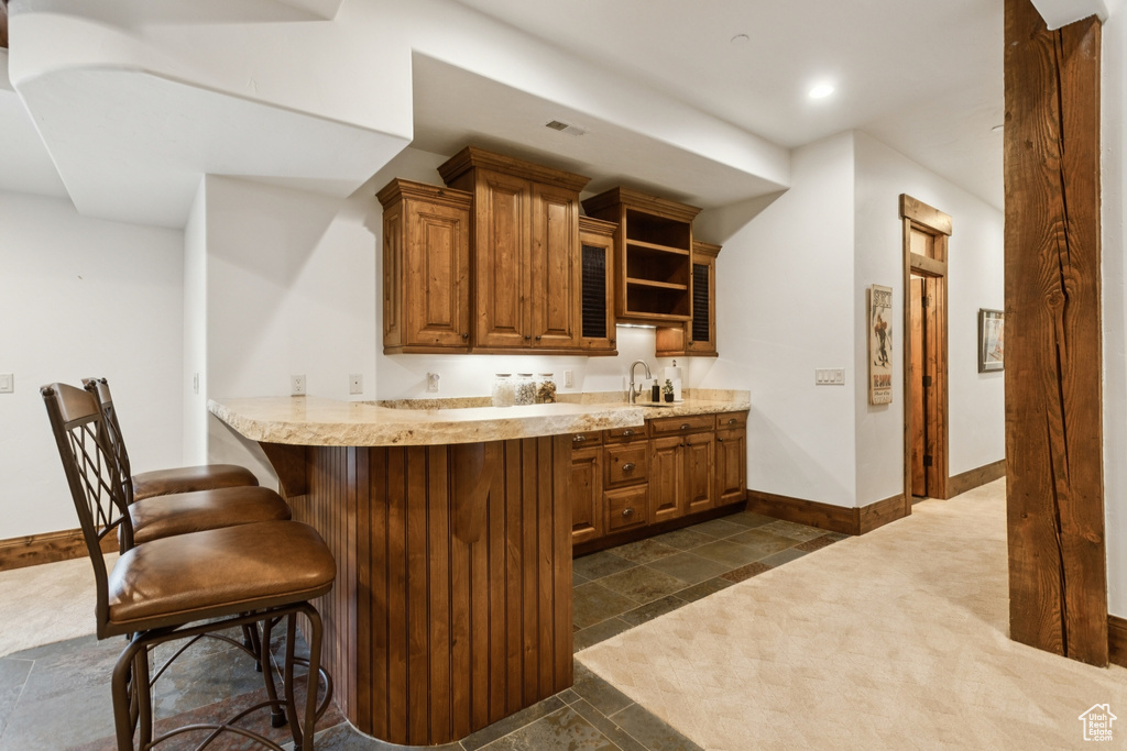 Kitchen with brown cabinets, a breakfast bar area, open shelves, light stone counters, and recessed lighting