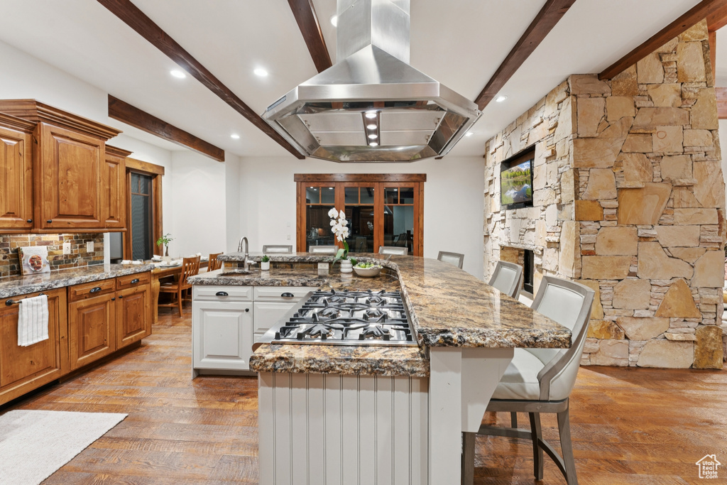 Kitchen featuring island exhaust hood, stainless steel gas stovetop, beamed ceiling, light wood finished floors, and a large island