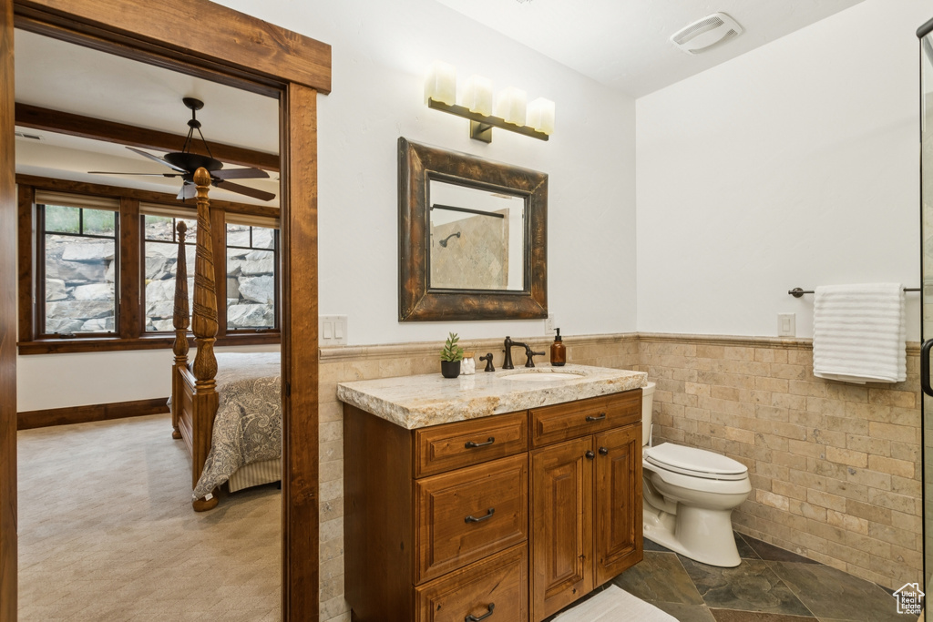 Bathroom with a ceiling fan, vanity, tile walls, wainscoting, and ensuite bathroom
