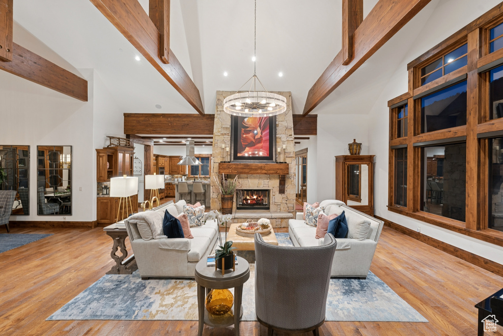 Living area with high vaulted ceiling, a chandelier, beamed ceiling, a stone fireplace, and wood finished floors
