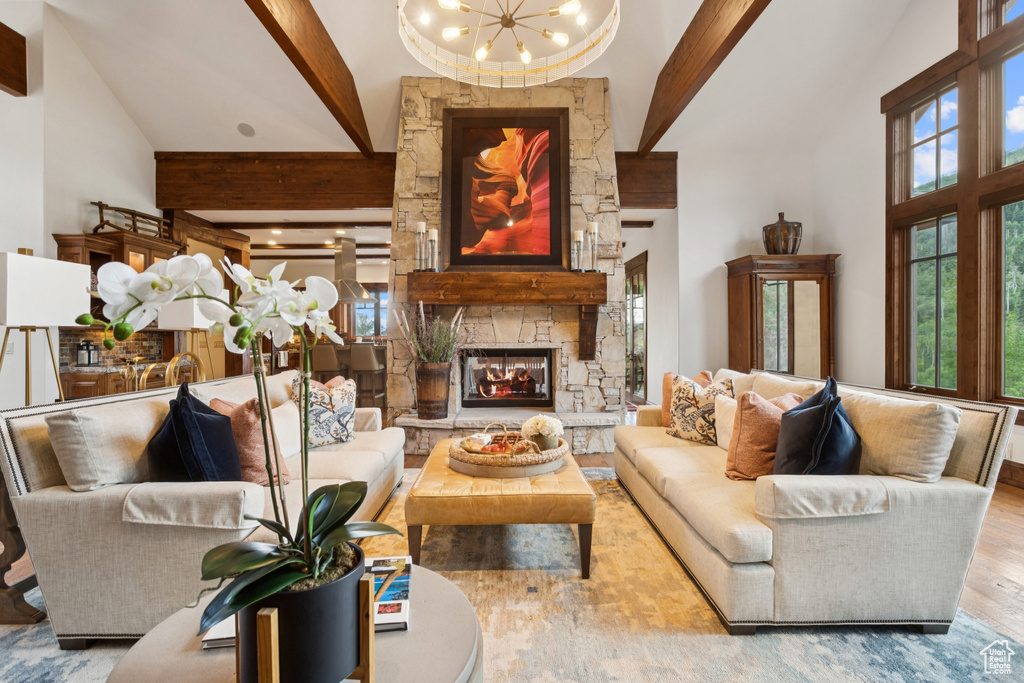 Living room with high vaulted ceiling, beamed ceiling, a chandelier, a stone fireplace, and wood finished floors