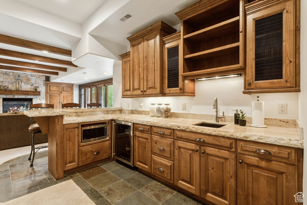 Kitchen with wine cooler, stainless steel microwave, a breakfast bar area, a peninsula, and brown cabinetry