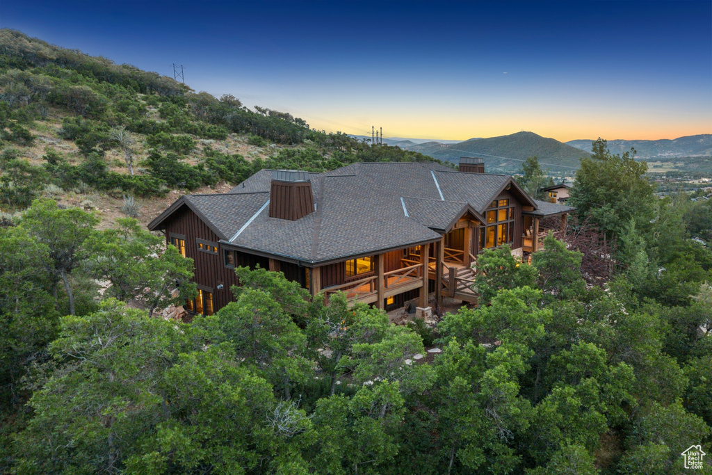 Back of house at dusk with a shingled roof, a mountain view, board and batten siding, a chimney, and covered porch