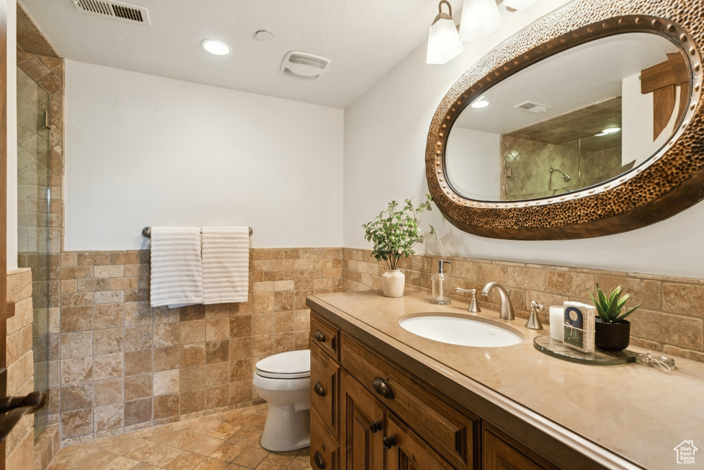 Bathroom with tile walls, vanity, a wainscoted wall, tiled shower, and recessed lighting